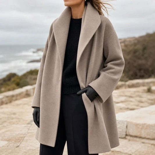 Oversized taupe coat with wide lapels and long sleeves, worn open with black gloves.