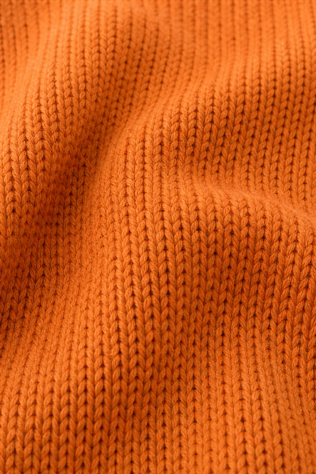 Close-up of orange knit pullover stitch texture and seams