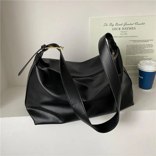 Black leather slouchy shoulder tote bag with metal clasp and long strap.