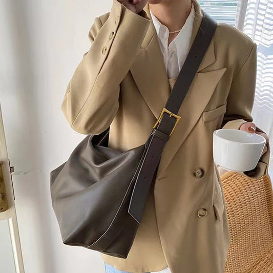 Slouchy gray leather shoulder tote bag worn crossbody with wide strap and buckle