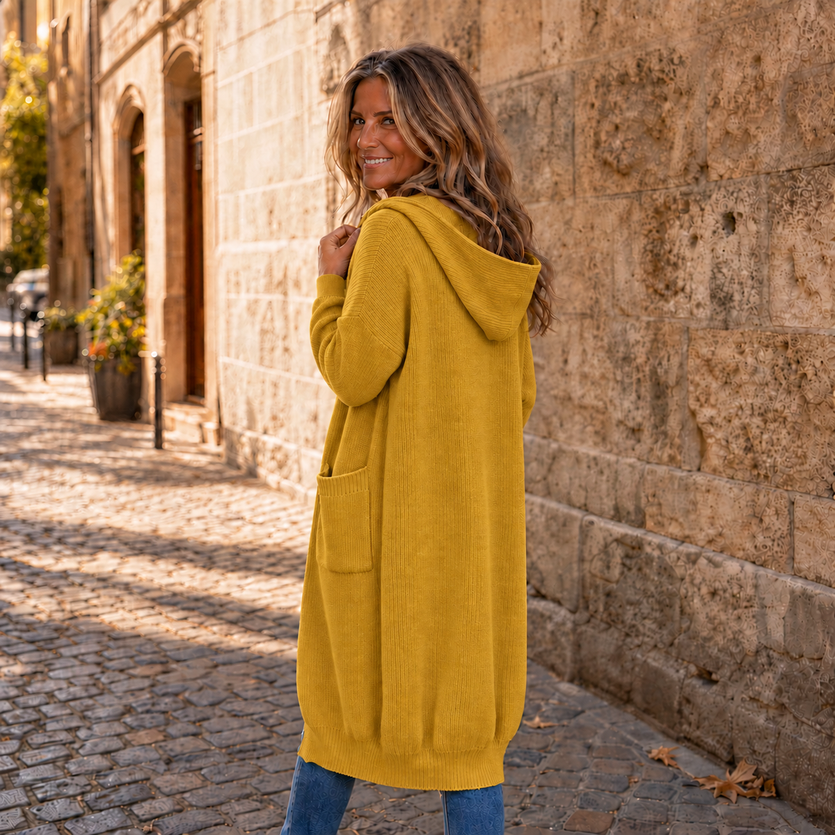 Back view of long yellow hooded cardigan with ribbed hem and a side pocket