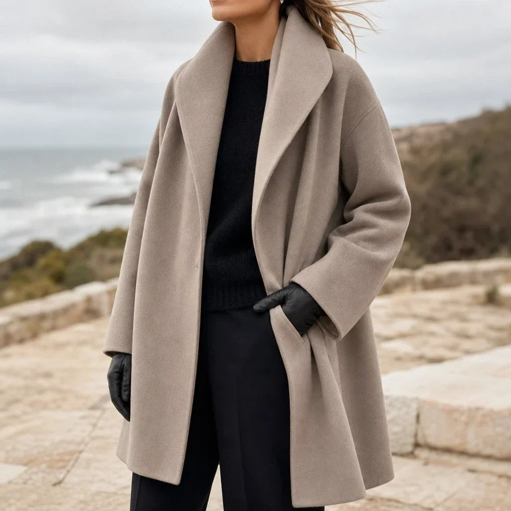 Oversized taupe coat with wide lapels and long sleeves, worn open with black gloves.