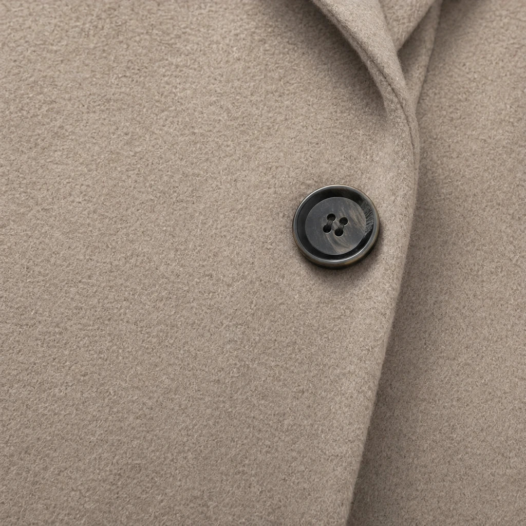 Taupe coat close-up showing a dark four-hole front button and textured fabric.
