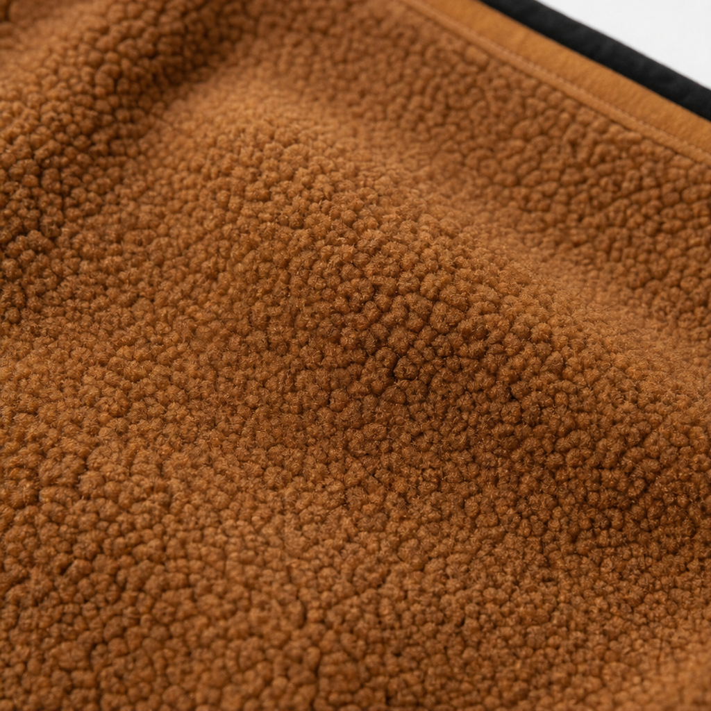 Brown sherpa fleece fabric close-up with soft textured surface and top stitching edge