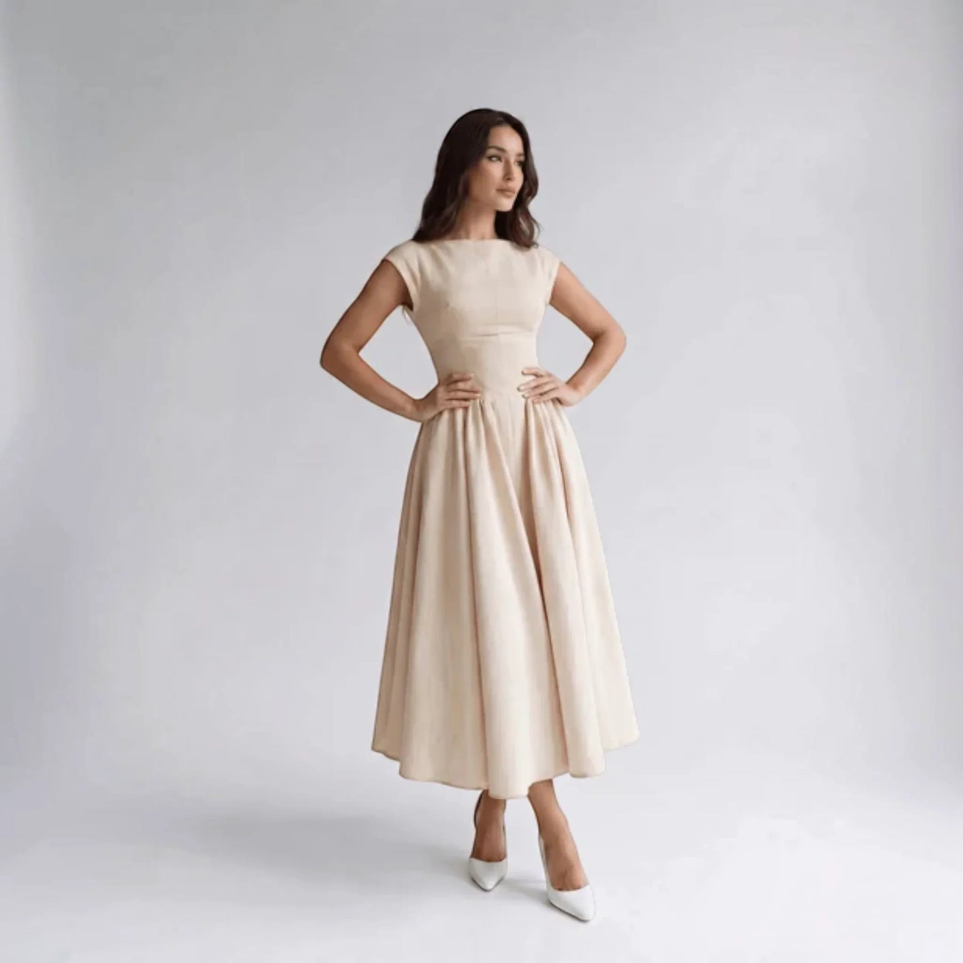 Beige sleeveless fit-and-flare midi dress, front with hands on hips and pleated skirt