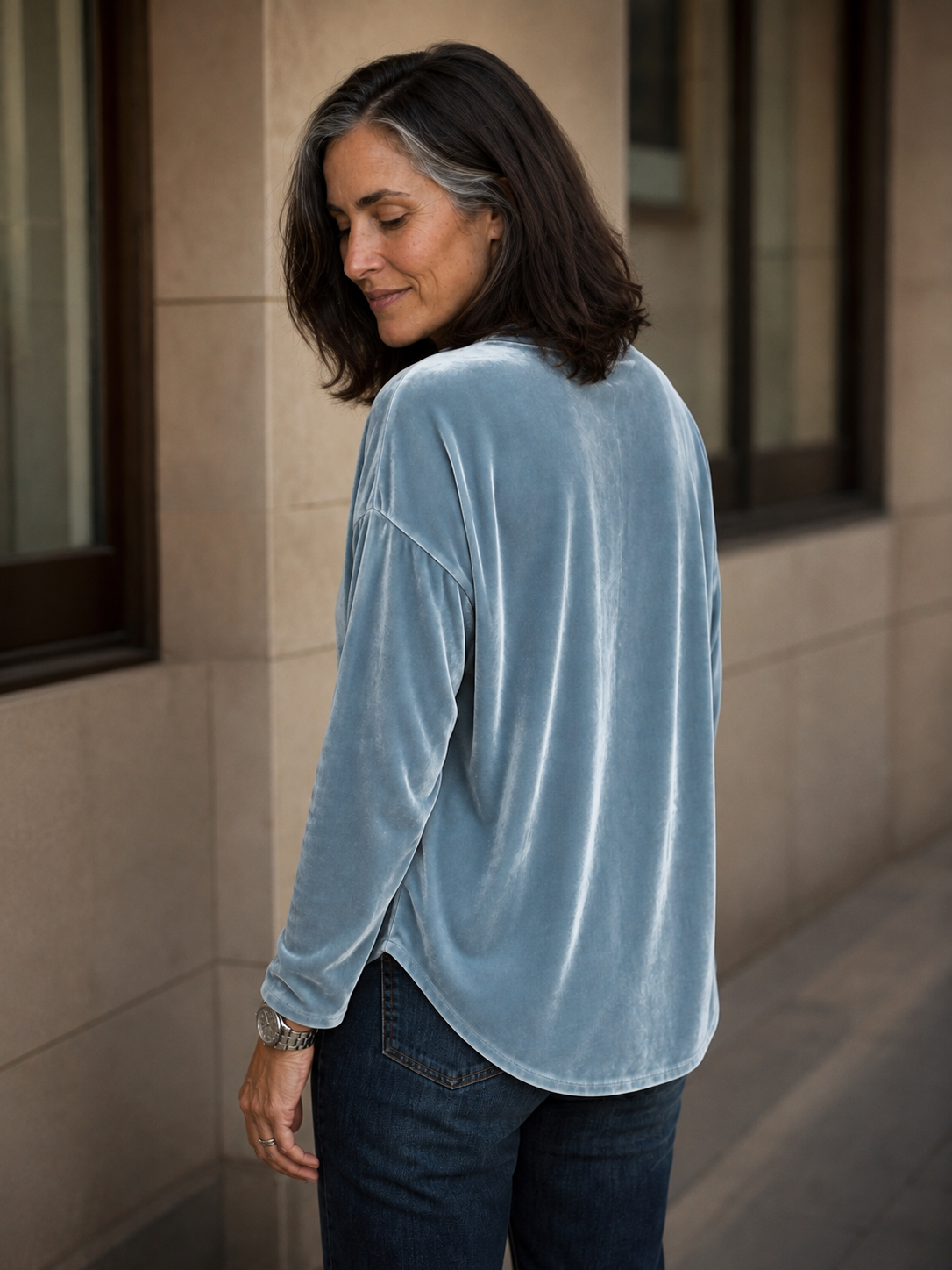 Back view of a light blue velvet blouse with a relaxed fit and curved hem