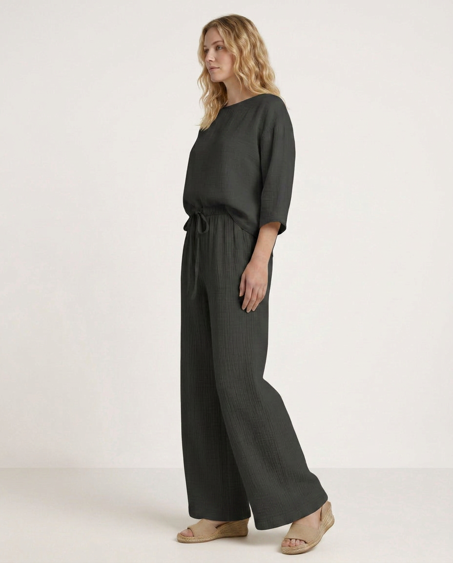 Wide-leg trousers with elastic waist and drawstring, dark gray fabric, side view.