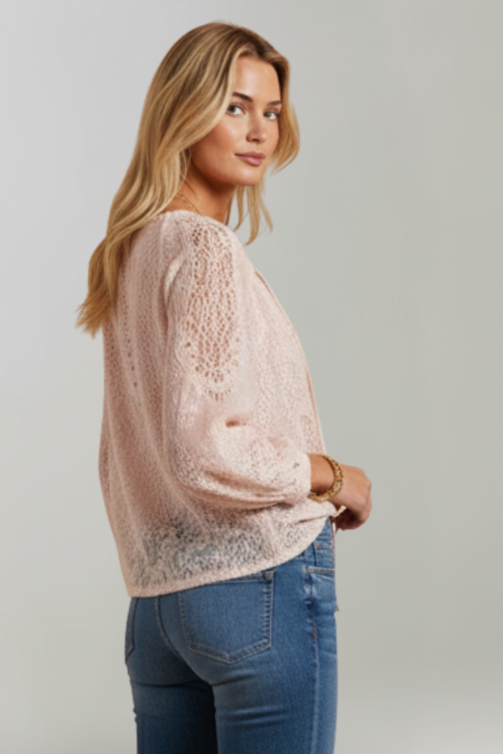 Pink lace blouse with tied V-neckline and textured lace long sleeves; side view